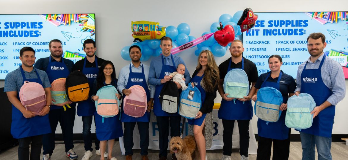 A group of people pose for picture holding backpacks and school supplies